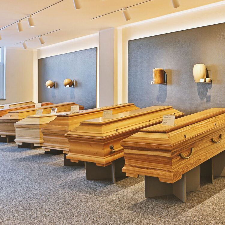 Mehrere Holzsärge stehen in einem gut beleuchteten Ausstellungsraum nebeneinander.