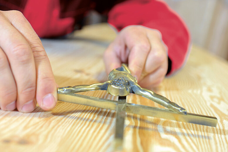 Eine Person bringt ein metallenes Kreuz auf einem Holzsarg an.