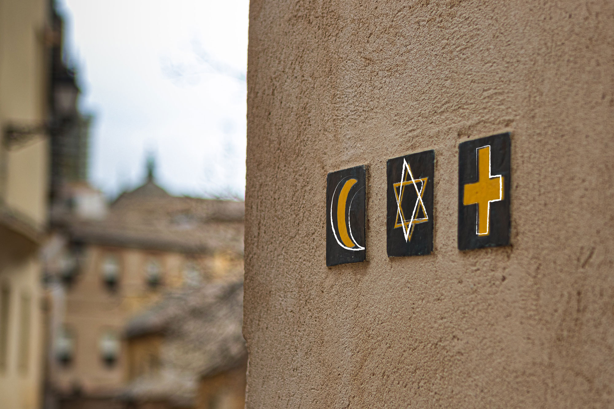 Auf einer Wand sind drei unterschiedliche Plaketten angebracht. Diese zeigen von links nach rechts einen Halbmond, ein Davidstern und ein Kreuz.